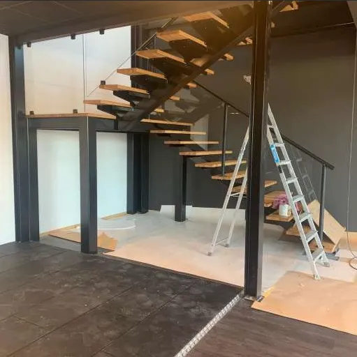 Modern svängd trappa under uppbyggnad med trästeg och stålbalk